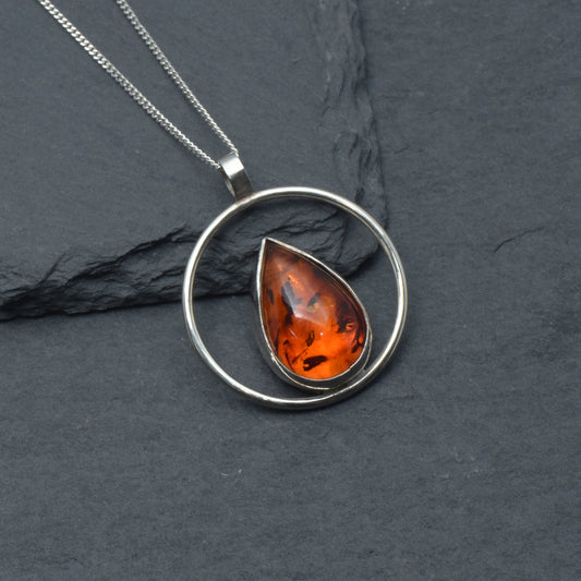 Tear drop Amber with a silver circle pendant on a slate background